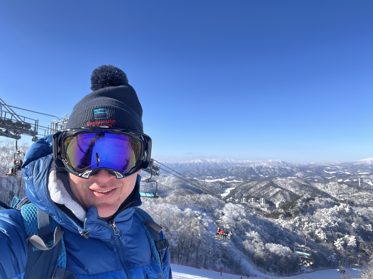 Standing at the summit of Mona Yongpyong Resort in South Korea, overlooking a breathtaking winter landscape with a chairlift and snow-covered mountains.