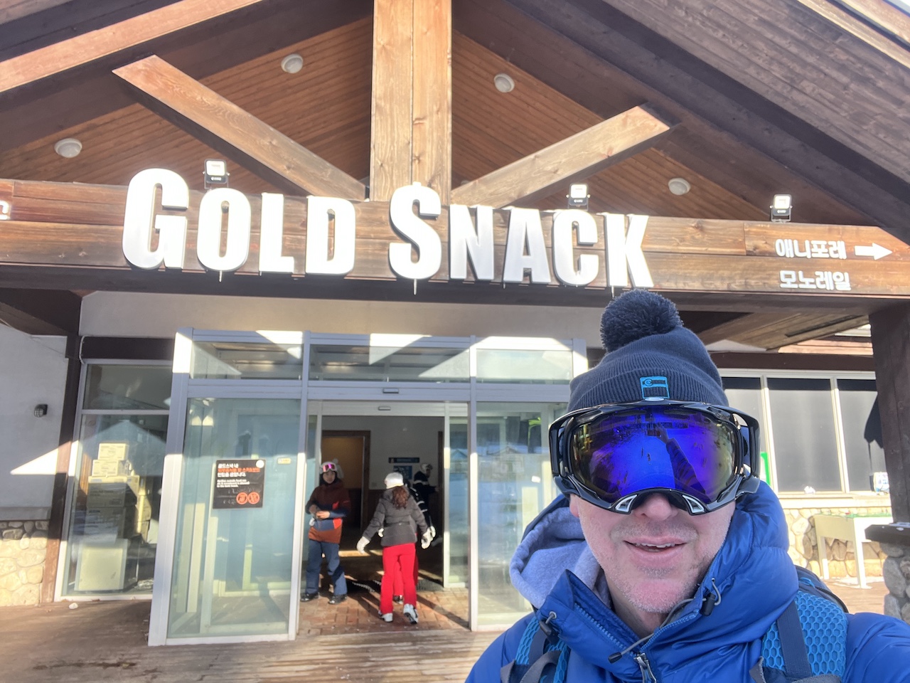 A skier poses in front of the Gold Snack lodge at Yongpyong Resort during ski season, with the lodge sign visible in the background.