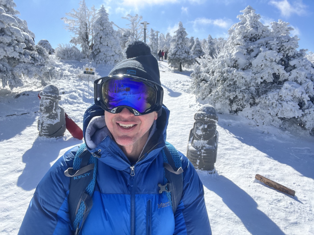 Skier standing in front of two snow-covered Jeju stone statues outside Dragon Castle in the Mona Park area of Yongpyong Resort during winter.