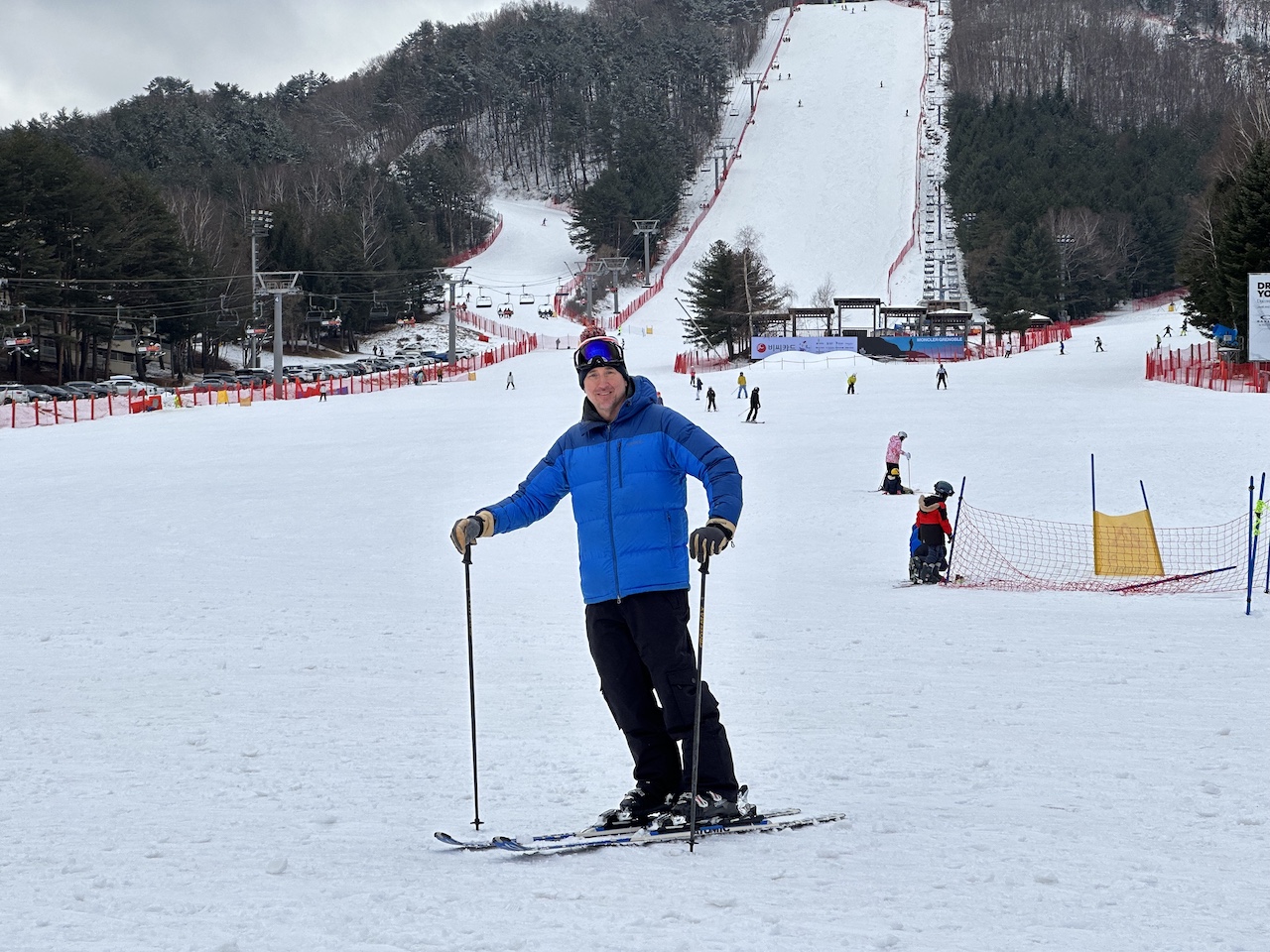 Skier standing at the base of the expert Red Trail in Yongpyong Resort's Red Zone, with the steep slope in the background, on a winter day.