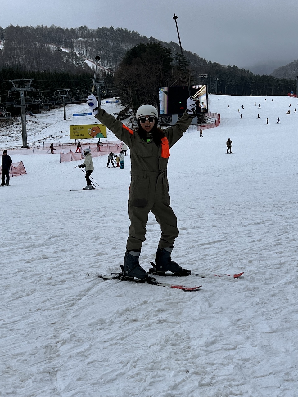 A Korean beginner skier wearing ski gear, posing happily at the base of the Silver Zone at Yongpyong Resort.