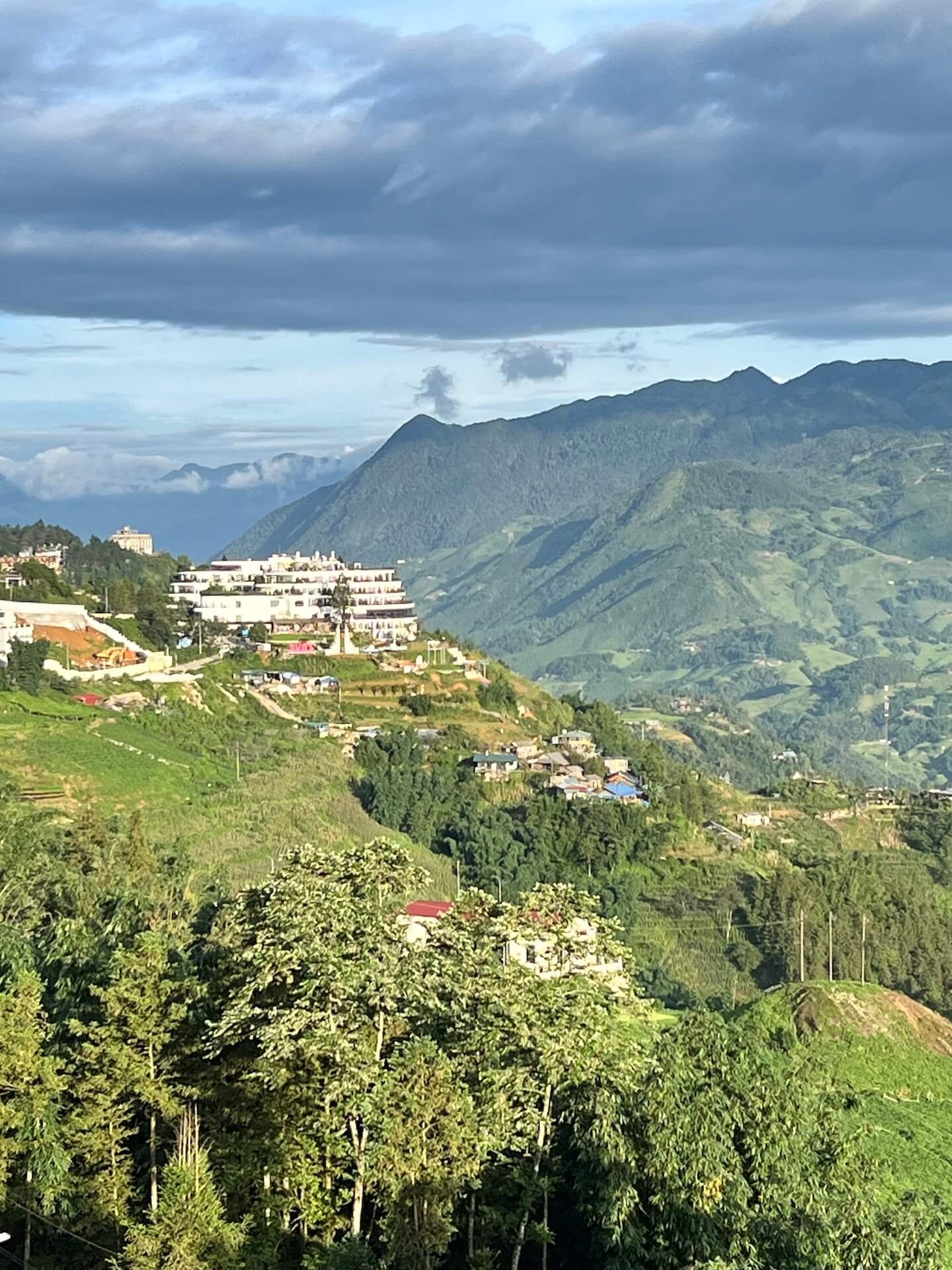 Pao’s Sapa Leisure Hotel, a white multi-level building, perched on a hillside with a stunning view of Sapa’s green mountains and valley.