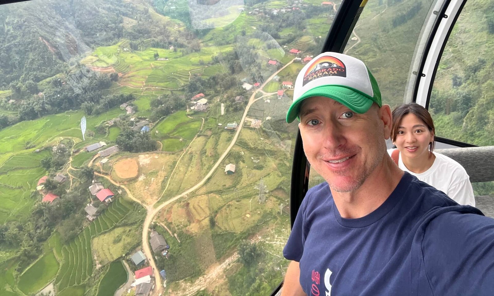 A couple inside an empty Fansipan cable car, surrounded by panoramic views of lush green mountains and small villages below, on their way to the peak in Sapa, Vietnam.