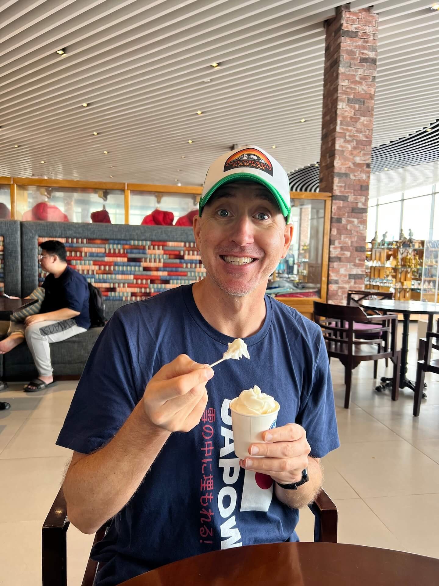 A man smiling while eating ice cream inside the cable car station at the top of Fansipan Peak in Sapa, Vietnam.