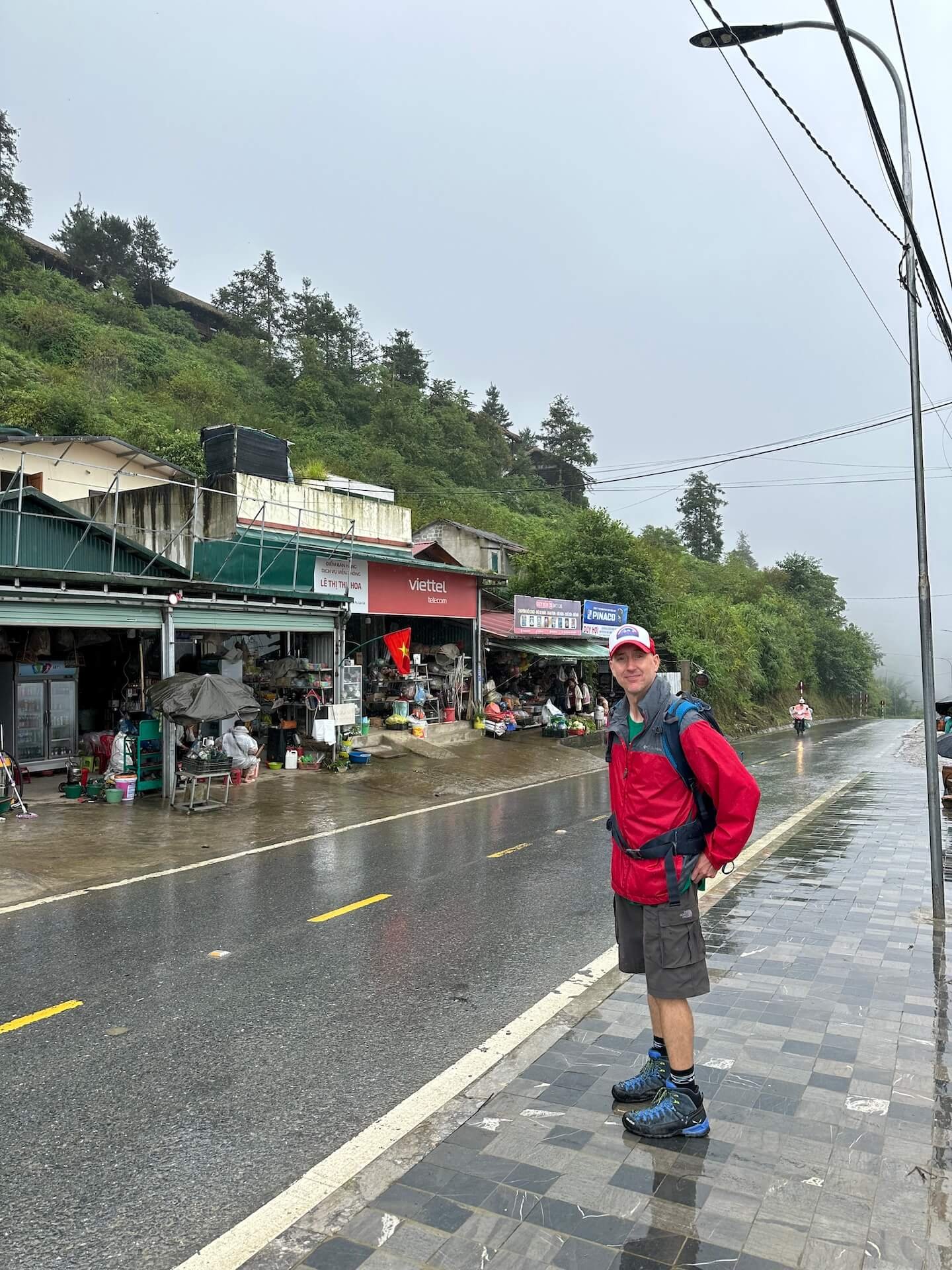 Traveler standing on a wet roadside in Sapa, Vietnam, at the starting point of a trekking route leading toward local villages and Sapa Clay House.