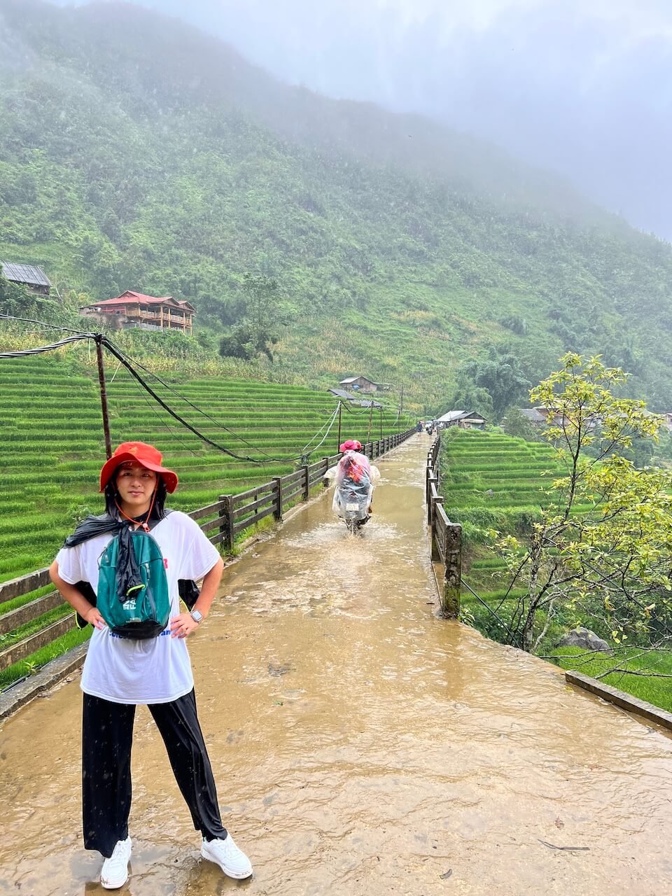 A trekker poses for a rainy photo in front of a bridge on the trek from Sapa to Lao Chai Village in Vietnam.