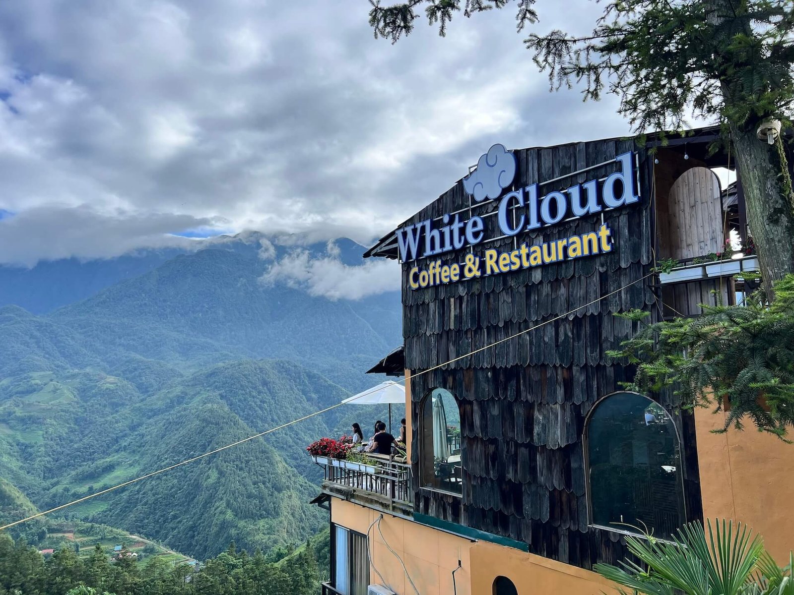 Exterior of White Cloud Coffee & Restaurant in Sapa, Vietnam, featuring a rustic wooden facade and a scenic mountain view in the background.