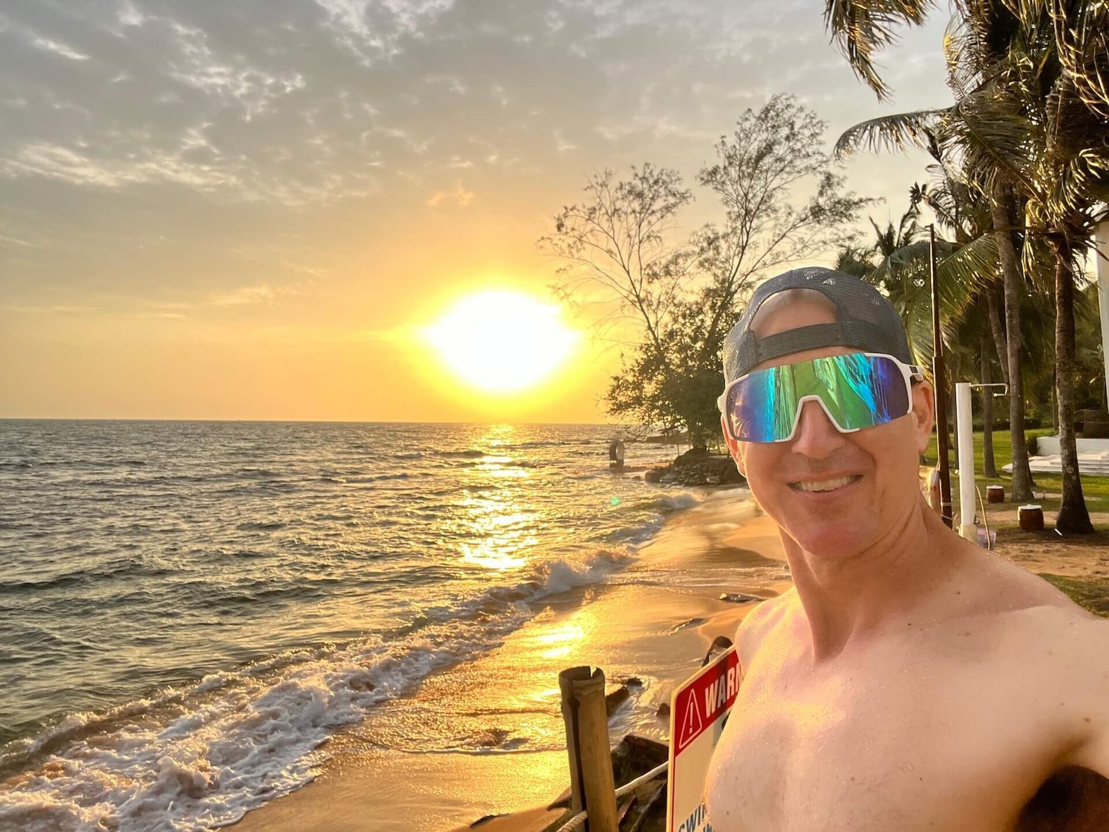 Traveler standing shirtless near the beach at sunset outside The Shells Resort in Phu Quoc, Vietnam, with waves and golden sky