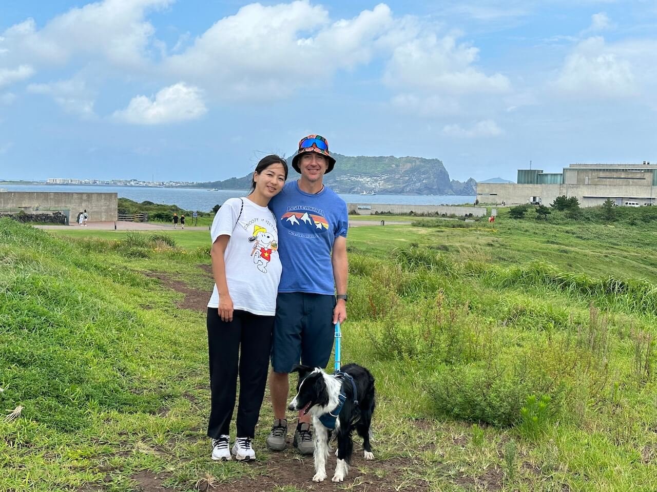 View of Seongsan Ilchulbong crater from a coastal field on Jeju Island with ocean in the background and people standing with a dog