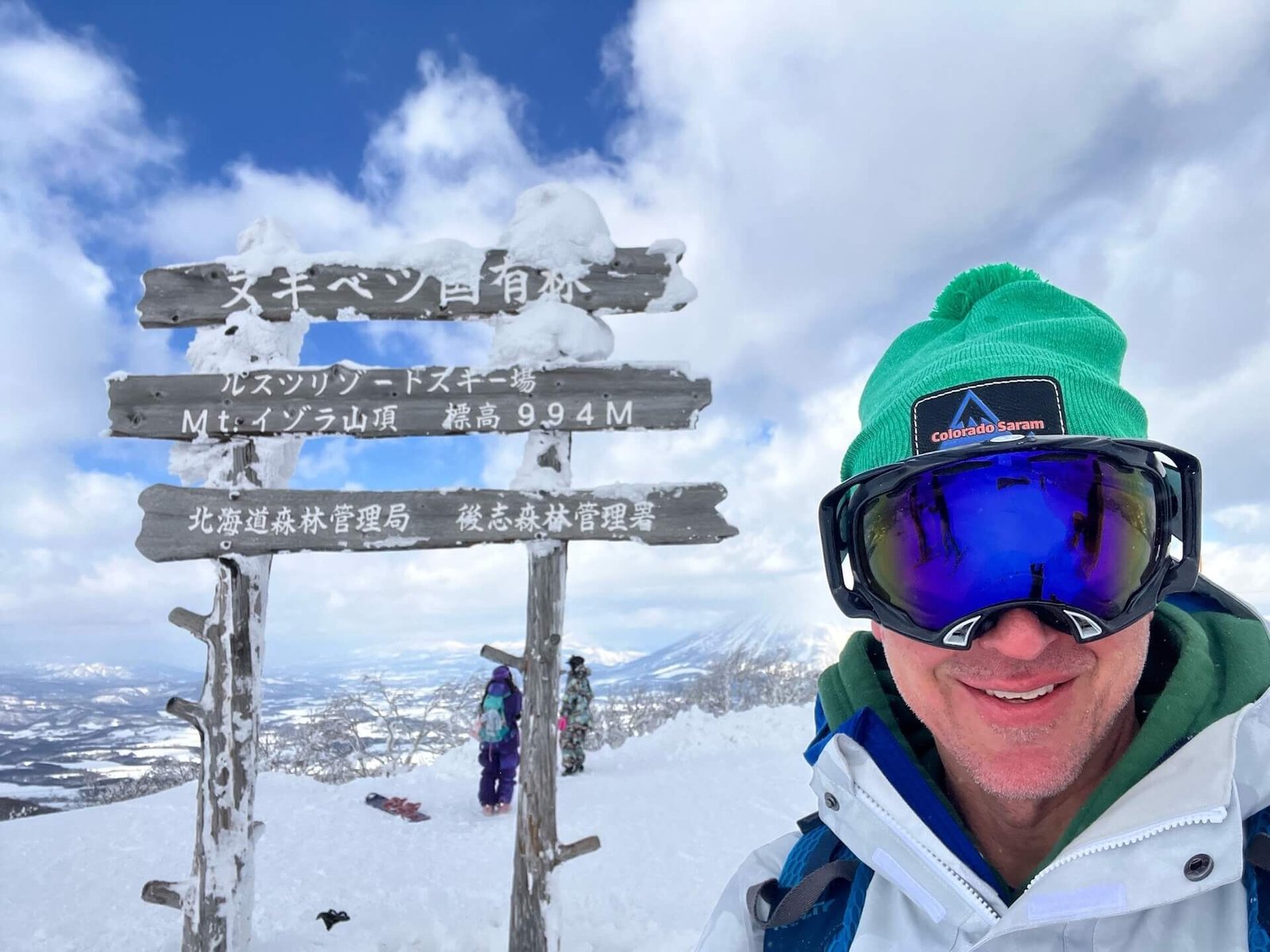 Smiling skier at the summit of Rusutsu Resort in Hokkaido, Japan, with snow-covered trail signs and panoramic views — Colorado Saram travel planning services