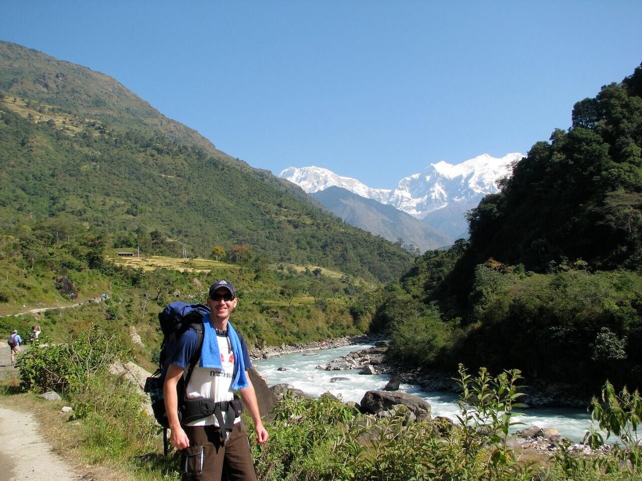 Annapurna Circuit vs Everest Base Camp: How to Choose the Right Nepal Trek 4 Trekker on the early Annapurna Circuit trail walking beside a river with snow-capped Himalayan peaks in the distance