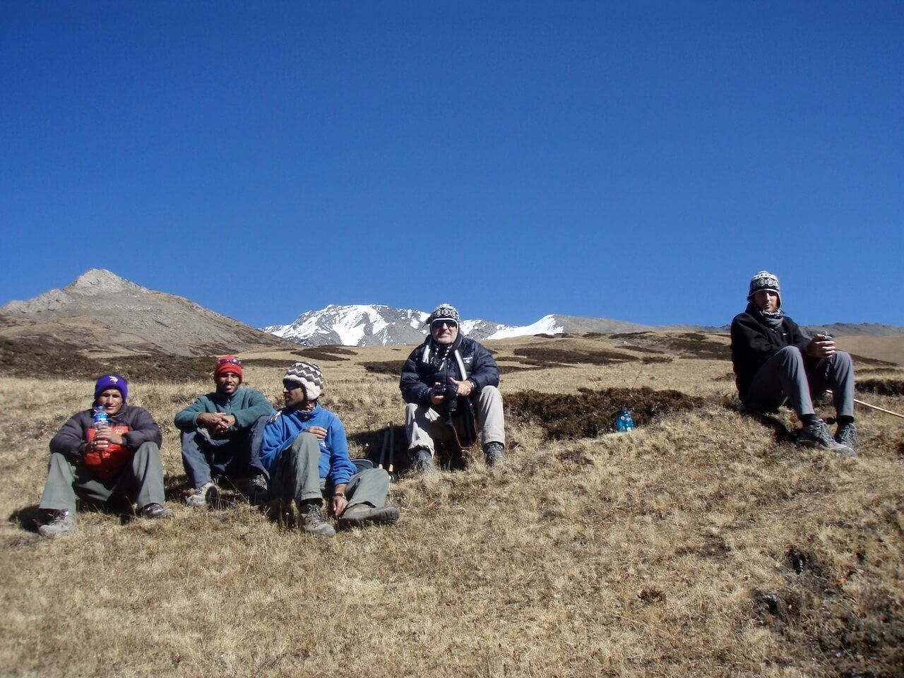 Annapurna Circuit vs Everest Base Camp: How to Choose the Right Nepal Trek 17 A group of Nepali guides and two Australian trekkers sitting on dry alpine grass beneath a clear sky, taking a break during an acclimatization day before crossing Thorong La Pass on the Annapurna Circuit.