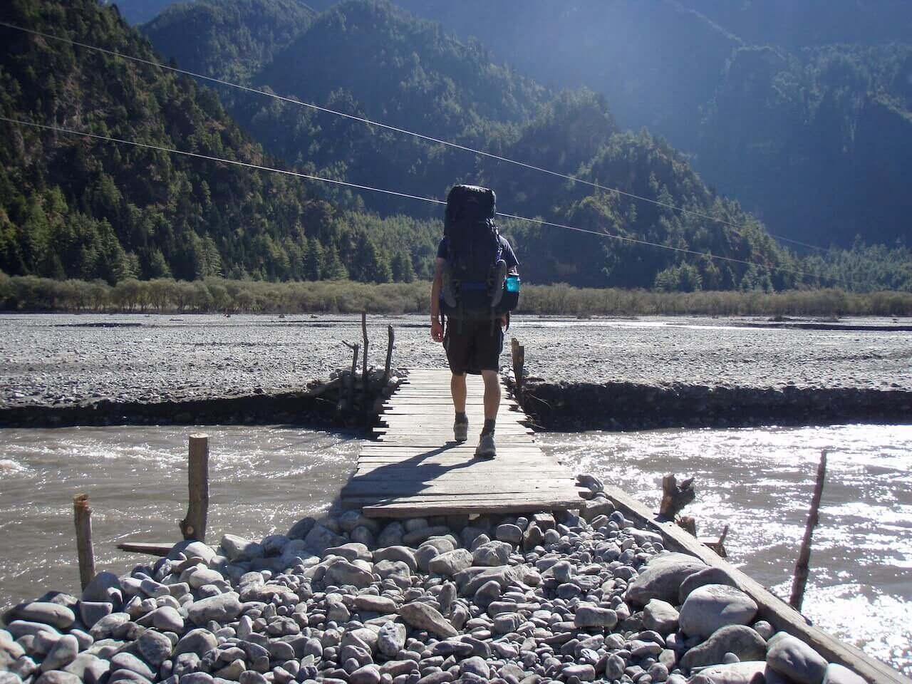 Annapurna Circuit vs Everest Base Camp: How to Choose the Right Nepal Trek 6 Backpacker crossing a wooden bridge over a river surrounded by forested hills after completing Thorong La Pass on the Annapurna Circuit