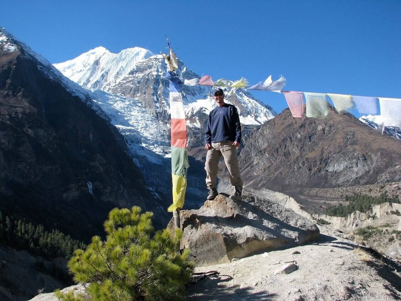 Annapurna Circuit vs Everest Base Camp: How to Choose the Right Nepal Trek 5 Trekker standing beside prayer flags with dramatic snow-capped mountains in the background on the Annapurna Circuit