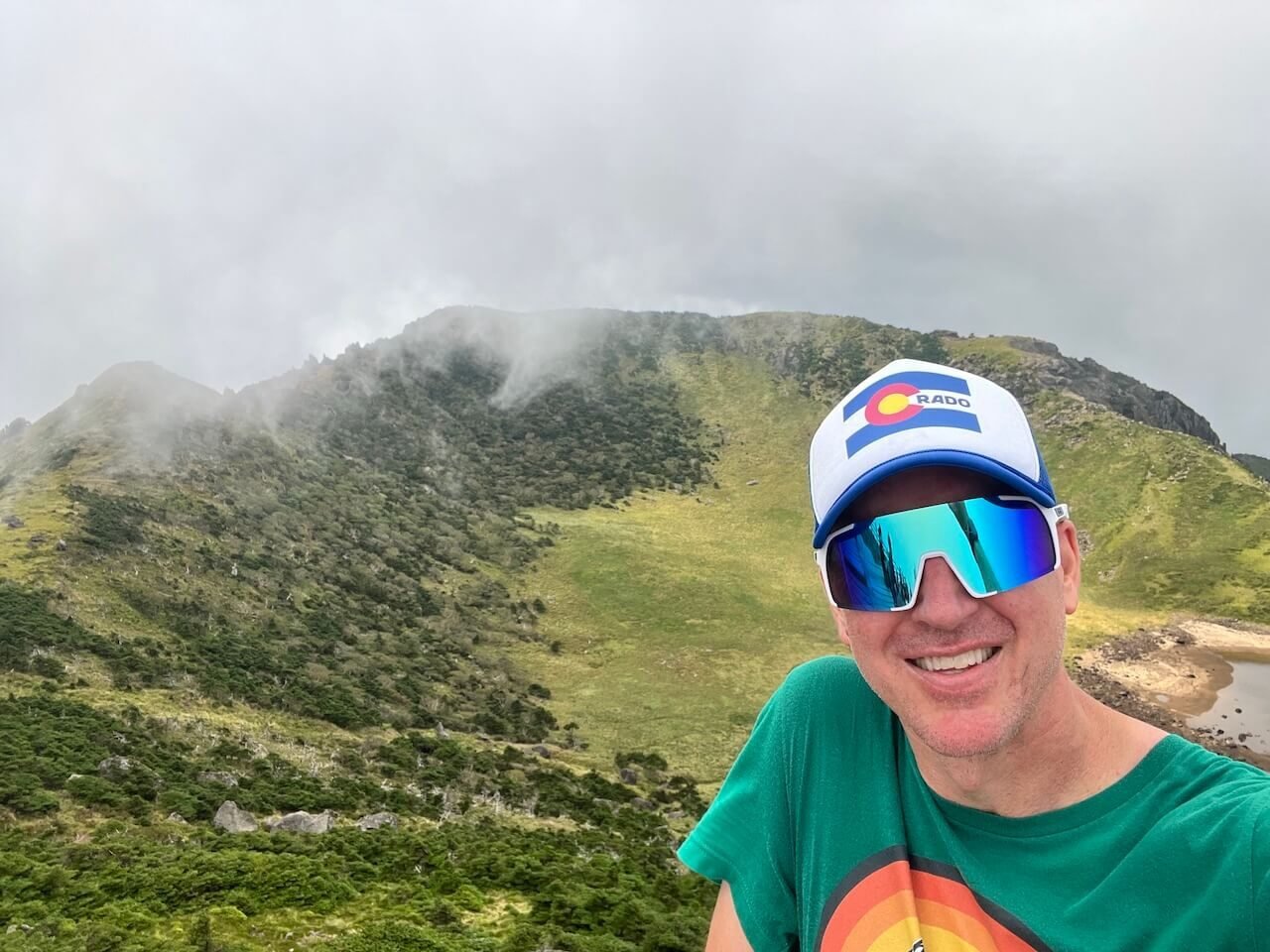 Why Climbing Hallasan in Summer Nearly Broke Me (And What I’d Do Differently) 12 Smiling hiker at the summit of Hallasan in Jeju, South Korea, with crater view and misty clouds in the background