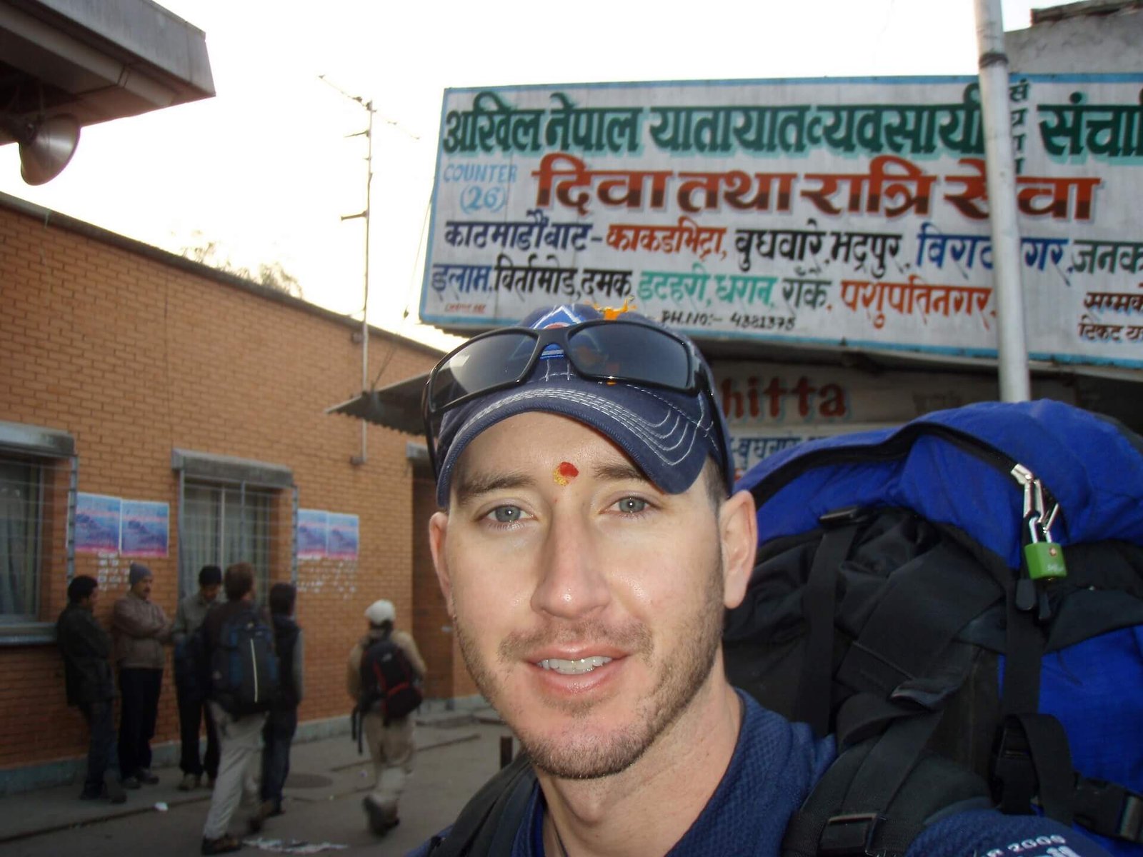 Annapurna Circuit vs Everest Base Camp: How to Choose the Right Nepal Trek 18 Backpacker with a red tika on his forehead and a large pack standing outside the busy tourist bus station in Kathmandu, preparing for the long ride to Besisahar.