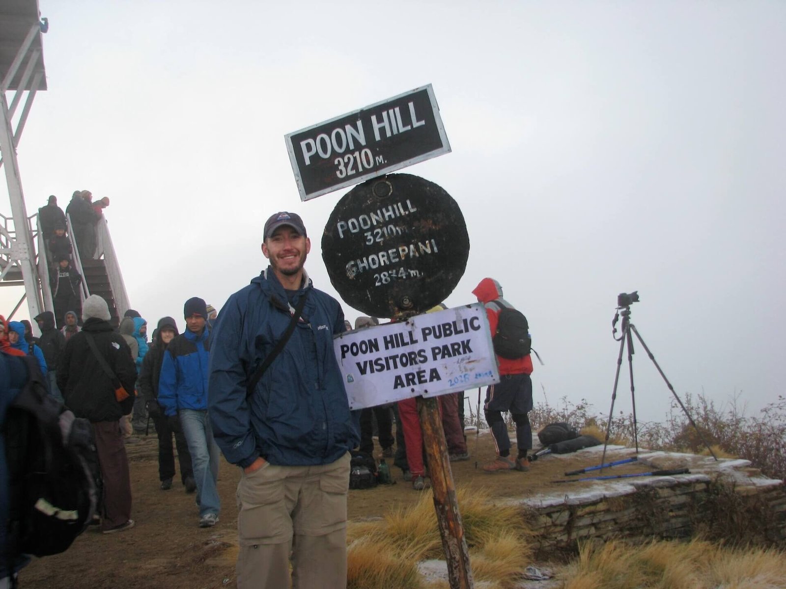 Annapurna Circuit vs Everest Base Camp: How to Choose the Right Nepal Trek 19 Trekker standing beside the Poon Hill summit sign at 3,210 meters, surrounded by hikers waiting for sunrise views on the Annapurna Circuit in Nepal.