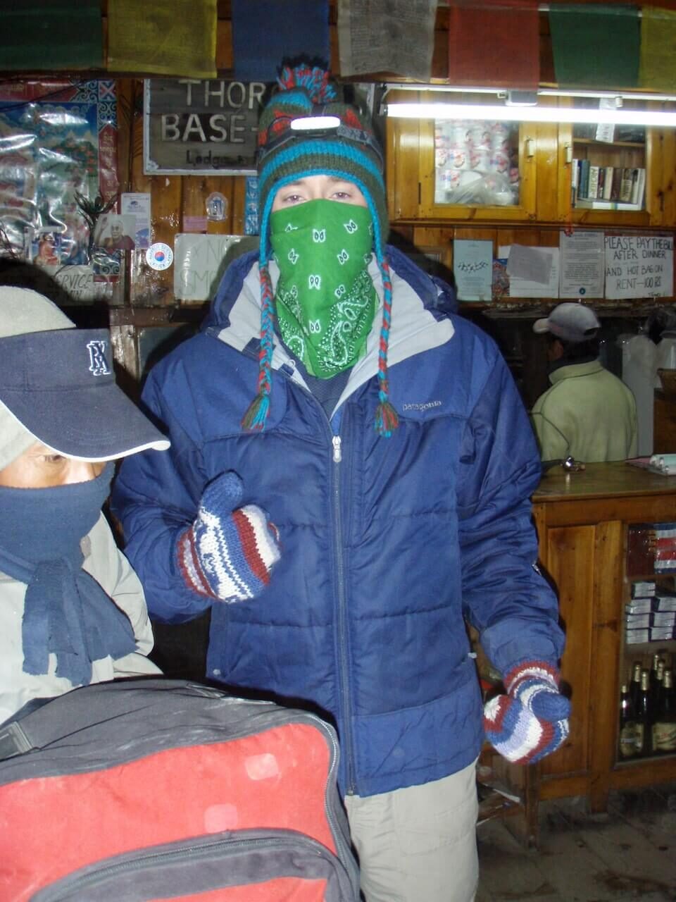 Annapurna Circuit vs Everest Base Camp: How to Choose the Right Nepal Trek 12 Bundled-up trekker wearing mittens, a headlamp, and face covering inside a lodge, preparing for the early morning ascent over Thorong La Pass on the Annapurna Circuit.