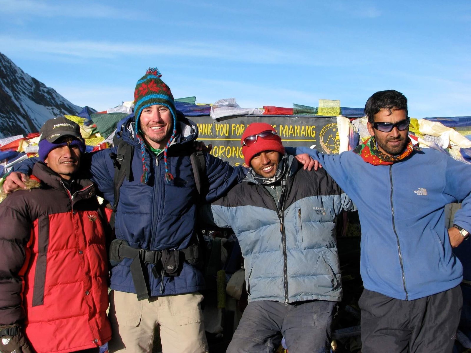 Annapurna Circuit vs Everest Base Camp: How to Choose the Right Nepal Trek 2 Group photo at Thorong La Pass on the Annapurna Circuit, with my guide Prakesh and two fellow trekkers' guides, standing in front of a wall of prayer flags