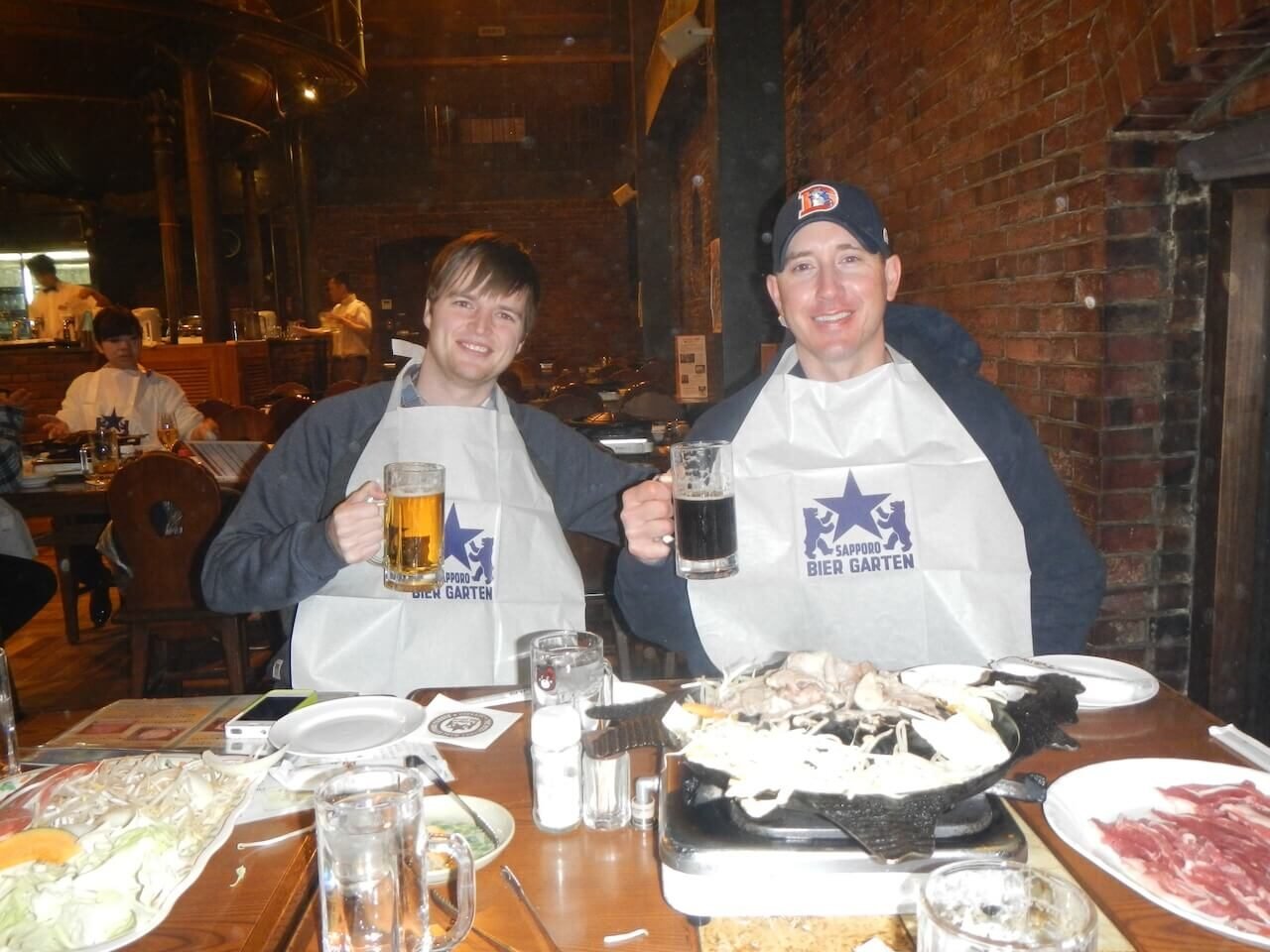 The Perfect 5–7 Day Hokkaido Ski Itinerary (2025 Guide) 11 Two friends enjoying Genghis Khan lamb BBQ and Sapporo Classic beer at the Sapporo Beer Garden inside the historic red-brick building in Japan