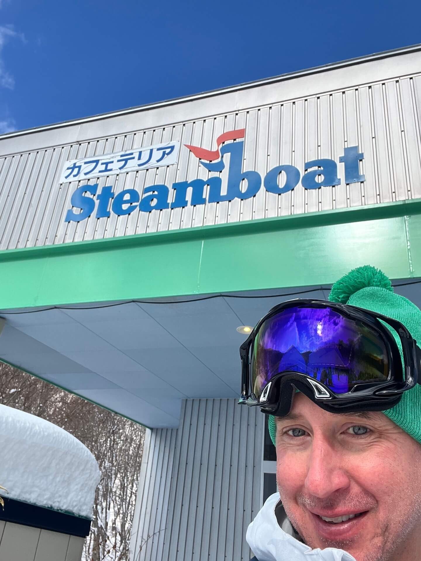 Smiling skier standing in front of the Rusutsu cafeteria building, which features the Steamboat name and logo on the sign.