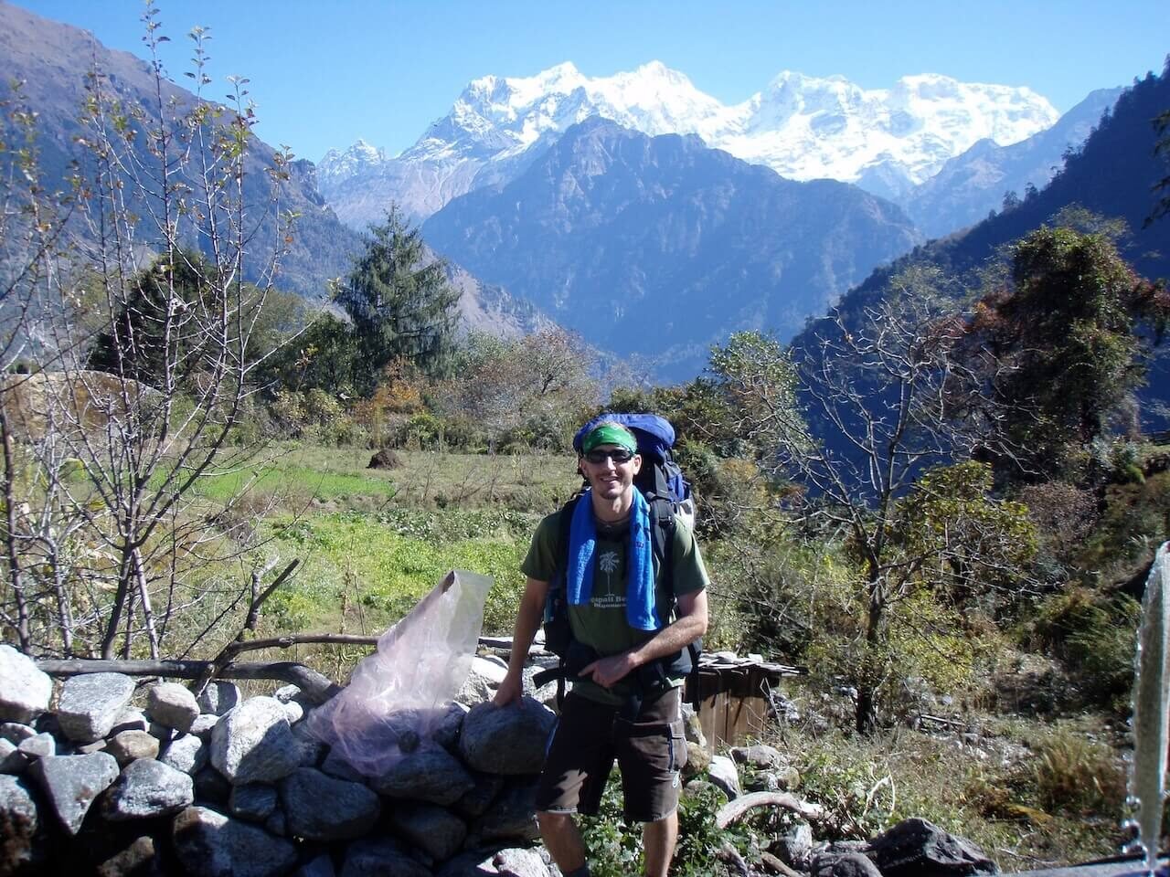 Man taking a break on a trekking trail in the Annapurna Circuit, Nepal, with a backpack on his shoulder and massive mountains surrounding him.