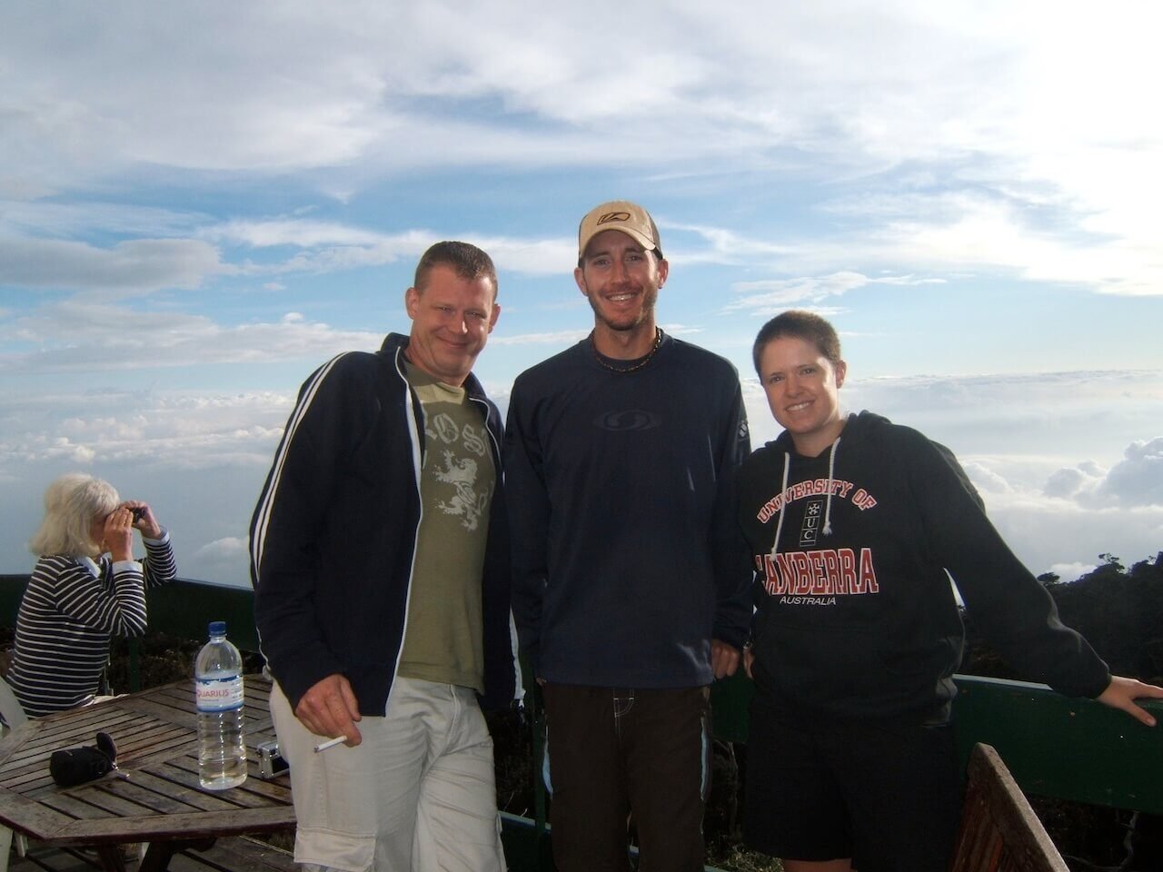 Man proudly displaying a Colorado flag patch on his backpack in front of a summit sign at Mount Kinabalu, Borneo.