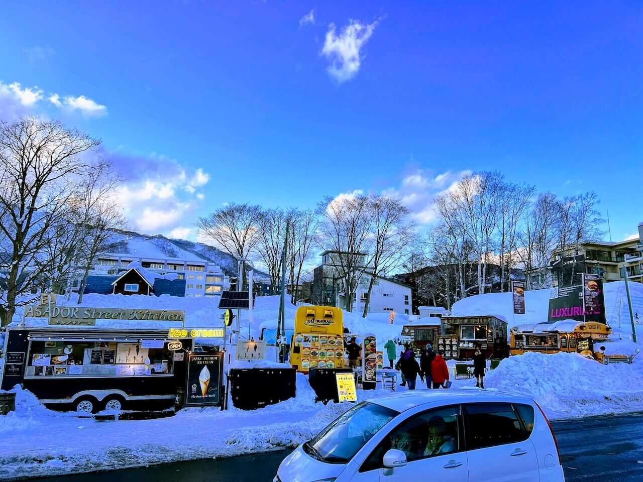 Food trucks and pedestrians near the central Niseko junction in winter, where foot traffic and cars mix on snowy streets