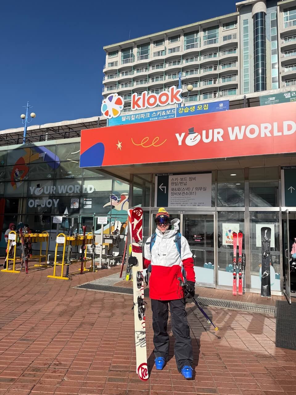 Skier standing at the base area of Welli Hilli holding skis before heading up for the first runs